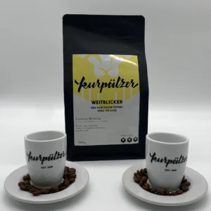 Zwei Tassen und Untertassen mit Kaffeebohnen neben einer schwarzen Tüte mit Geschenkpaket - Kirschblüte.